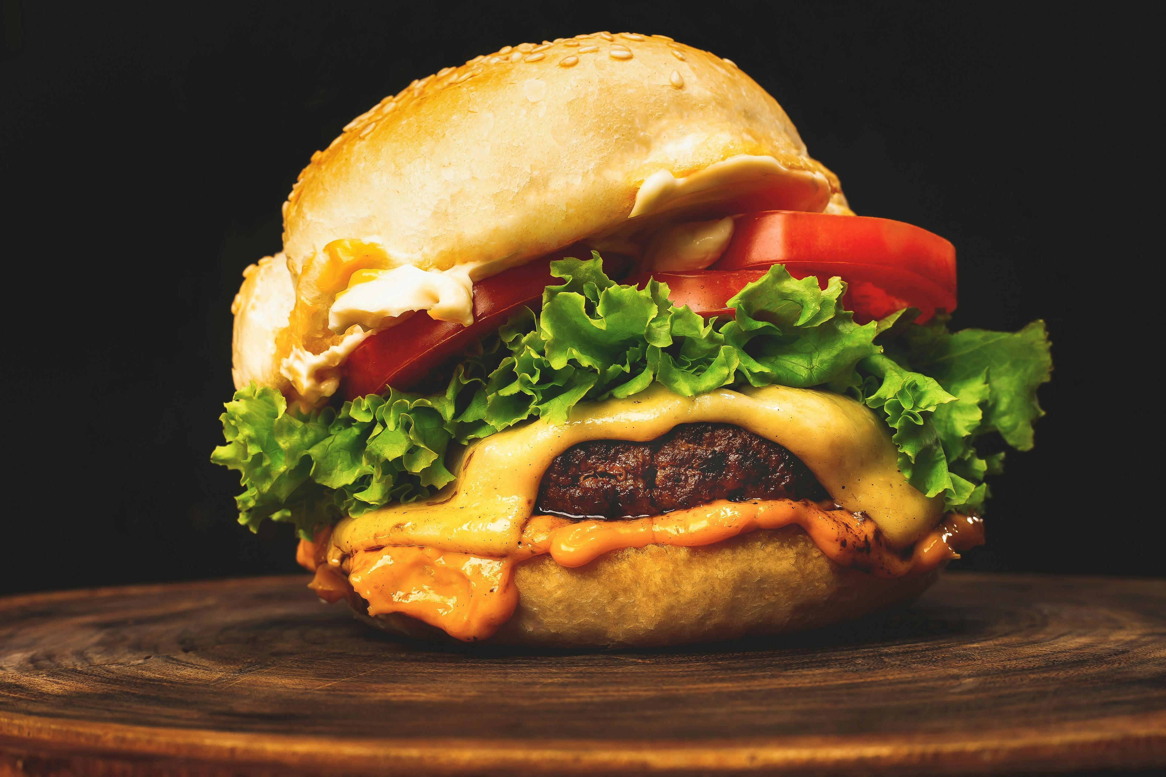 Photo of a hamburger on a wooden board with tomato, lettuce and cheese.
